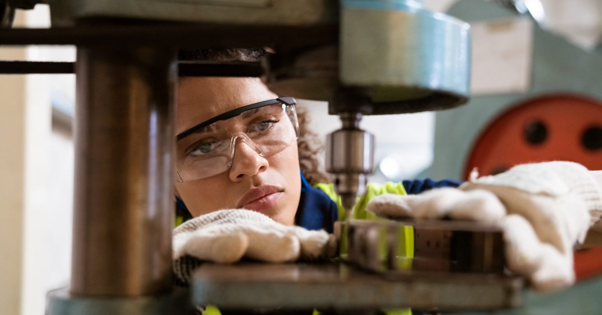 Close-up of female apprentice using yoke machine. Female engineer is wearing protective glasses in factory. She is working in manufacturing industry.